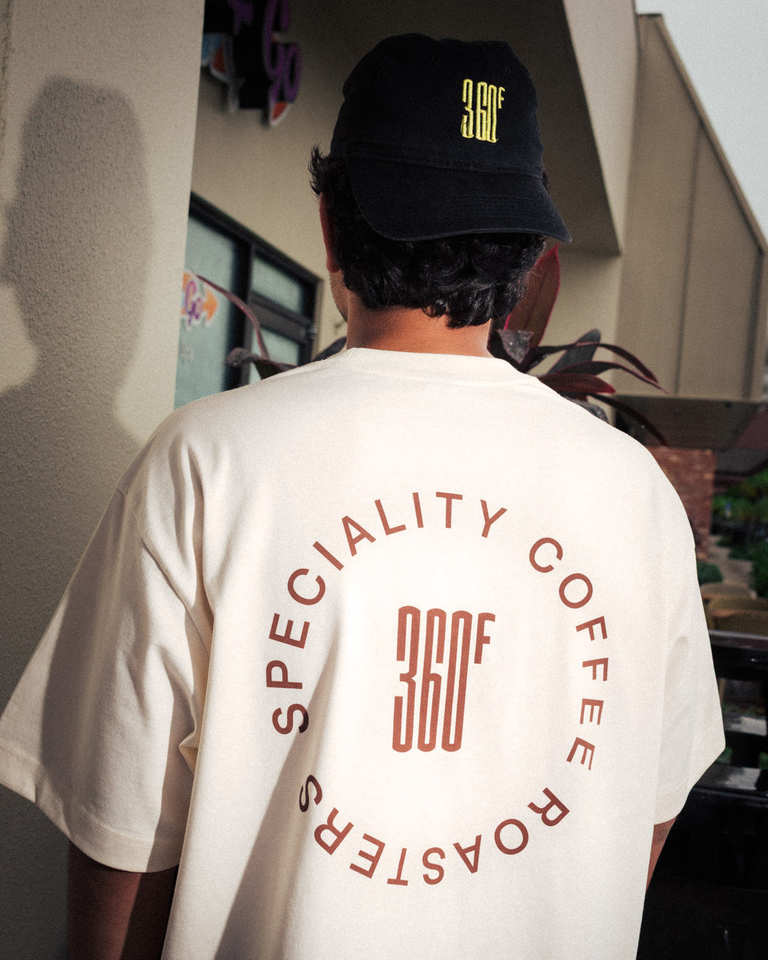 Person wearing a white t-shirt with 'Speciality Coffee Roasters' branding and a black cap.