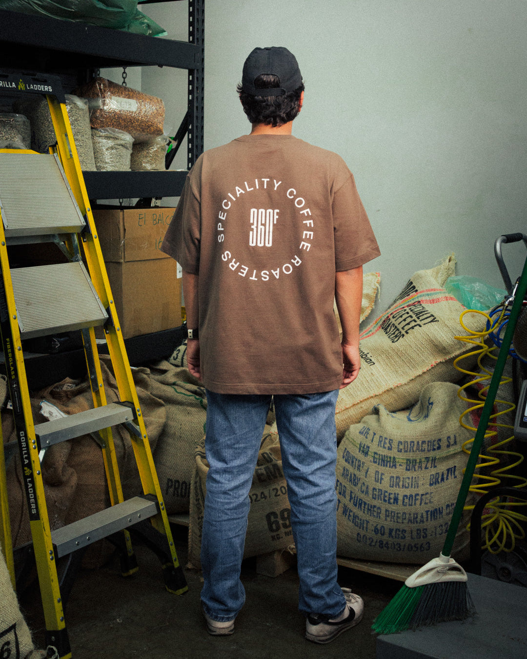 Person wearing a brown t-shirt with 'Specialty Coffee Roasters' logo in a storage room.