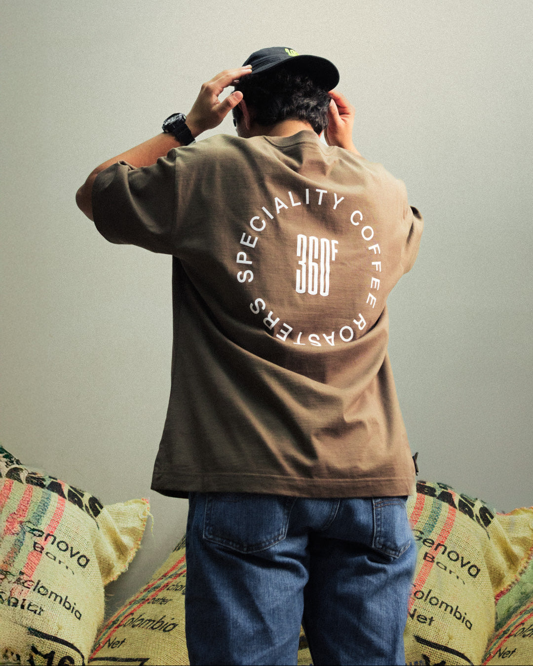 Person wearing a brown jacket with 'Specialty Coffee Roasters' branding, standing in front of coffee bags.