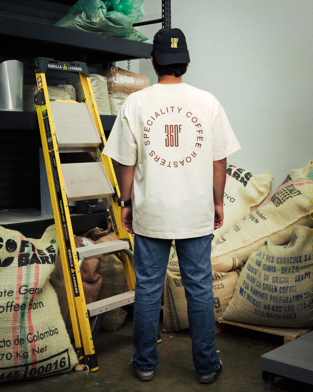 Person wearing a 'Specialty Coffee Roasters' t-shirt in a coffee roastery setting.