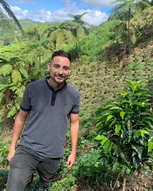 Man standing next to a coffee plant in a lush green forest